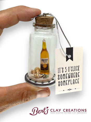 Miniature bottle with a Corona beer bottle inside, held by a hand, with a tag reading 'It's 5 o'clock somewhere someplace' by Berts Clay Creations.